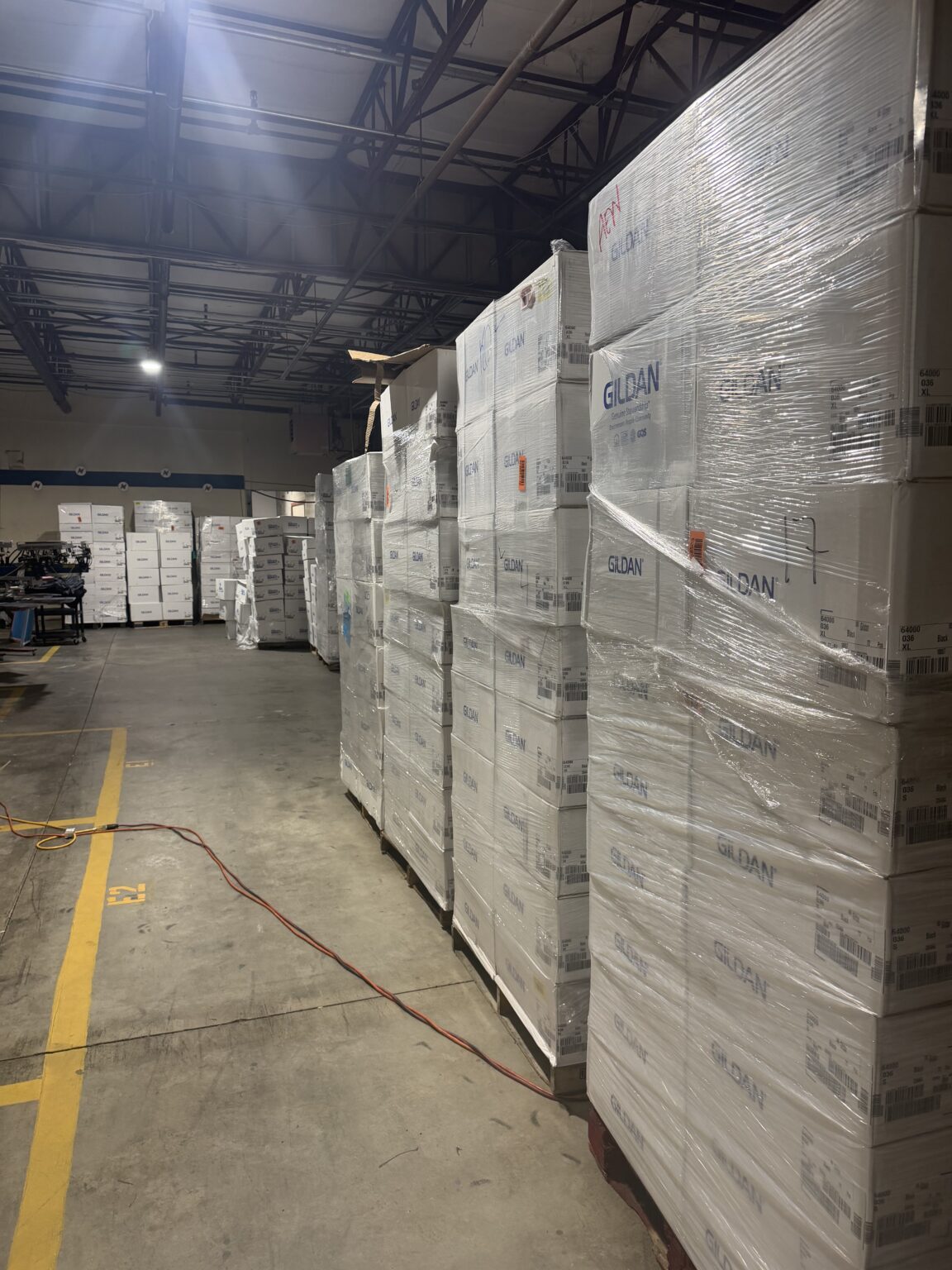 Pallets of shrink-wrapped Gildan Softstyle 64000 cases stacked in the 5Boys warehouse